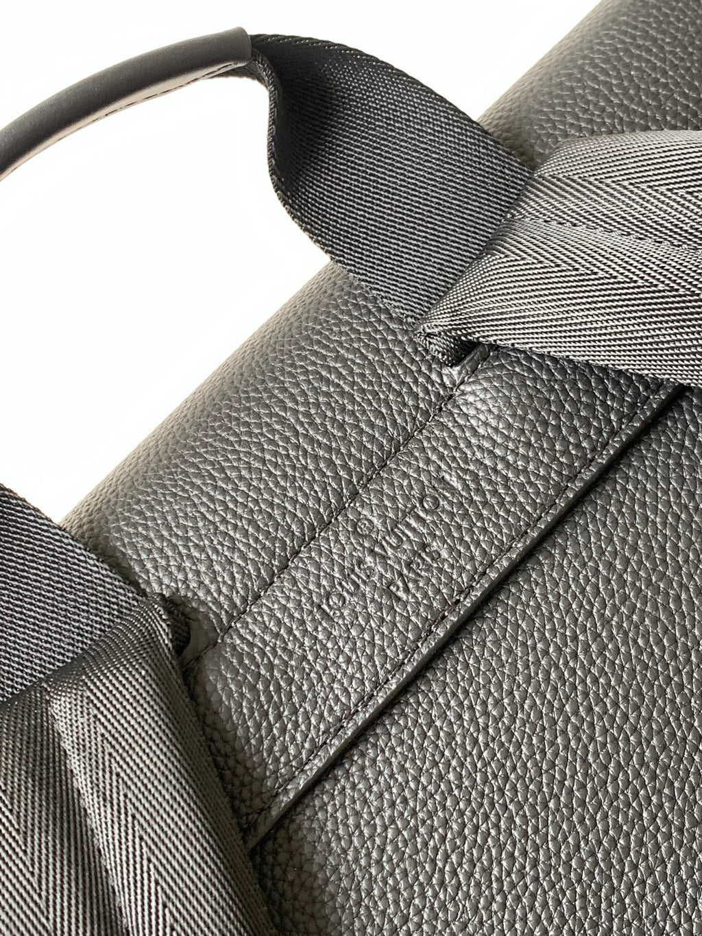 Men's Louis Vuitton bag close-up of strap attachment and textured leather detail, dark.