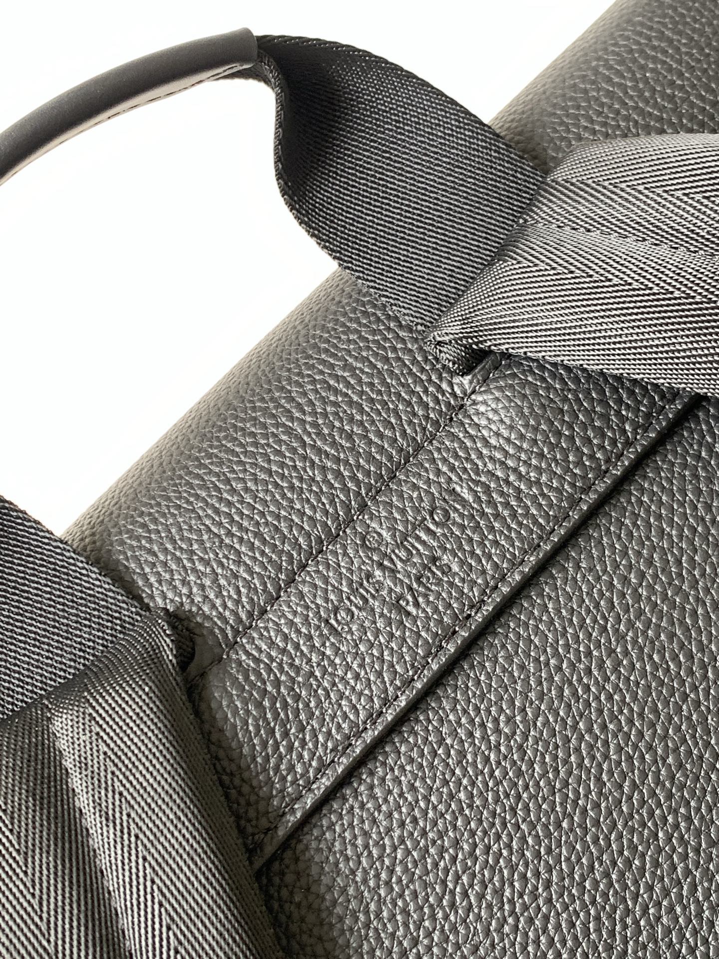Men's Louis Vuitton bag close-up of strap attachment and textured leather detail, dark.
