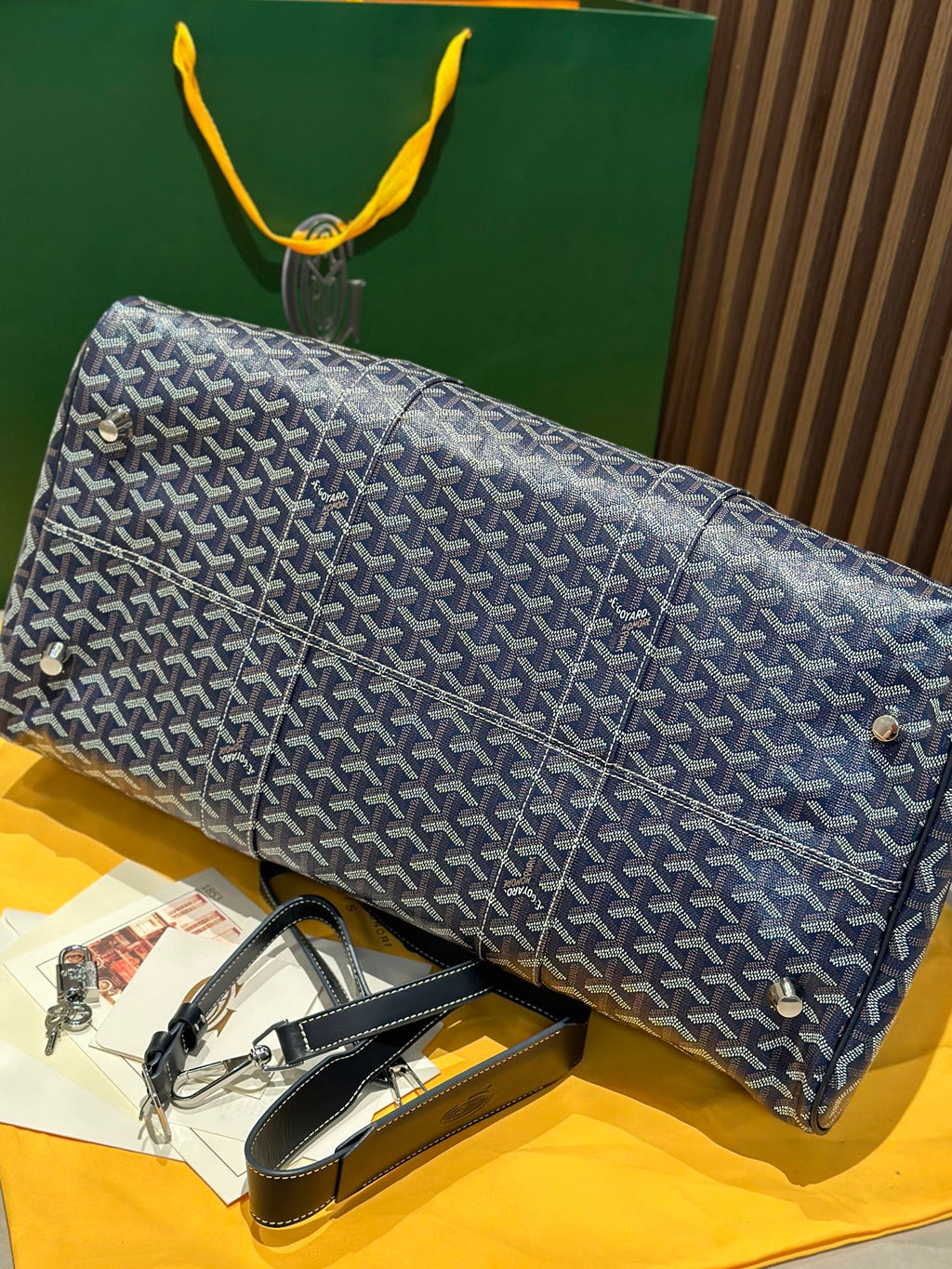 Goyard duffel bag laid on side with navy patterned canvas and rolled leather strap accents