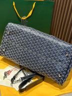 Goyard duffel bag laid on side with navy patterned canvas and rolled leather strap accents