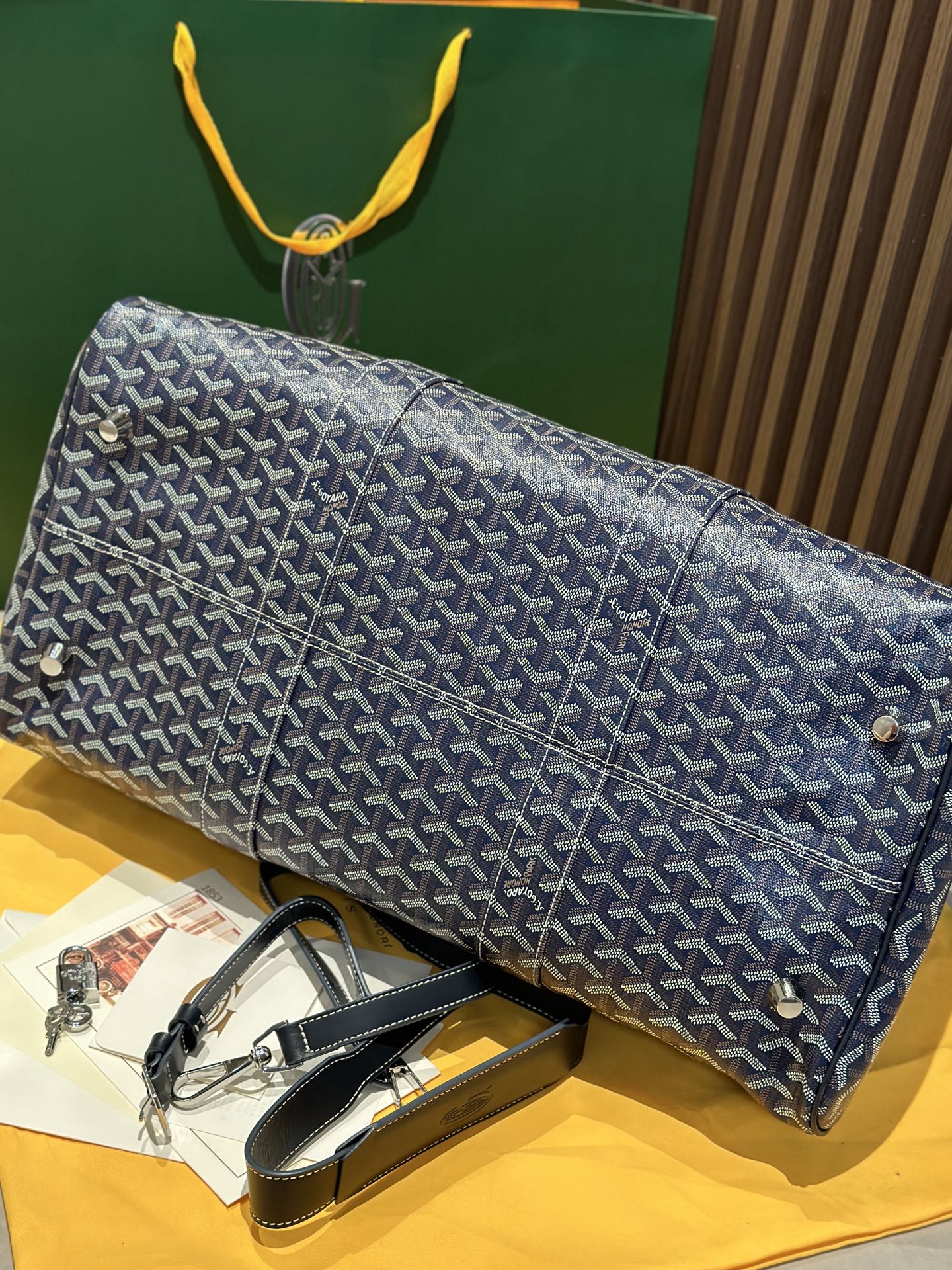 Goyard duffel bag laid on side with navy patterned canvas and rolled leather strap accents