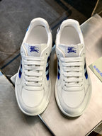 White leather sneakers with blue crest on tongue and lace-up front on display