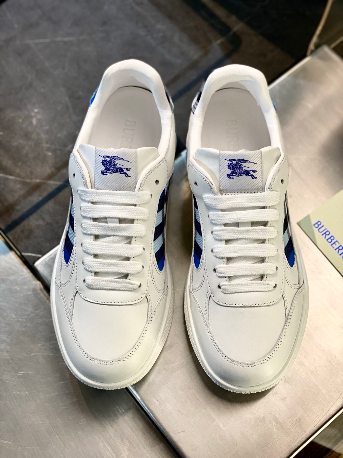 White leather sneakers with blue crest on tongue and lace-up front on display