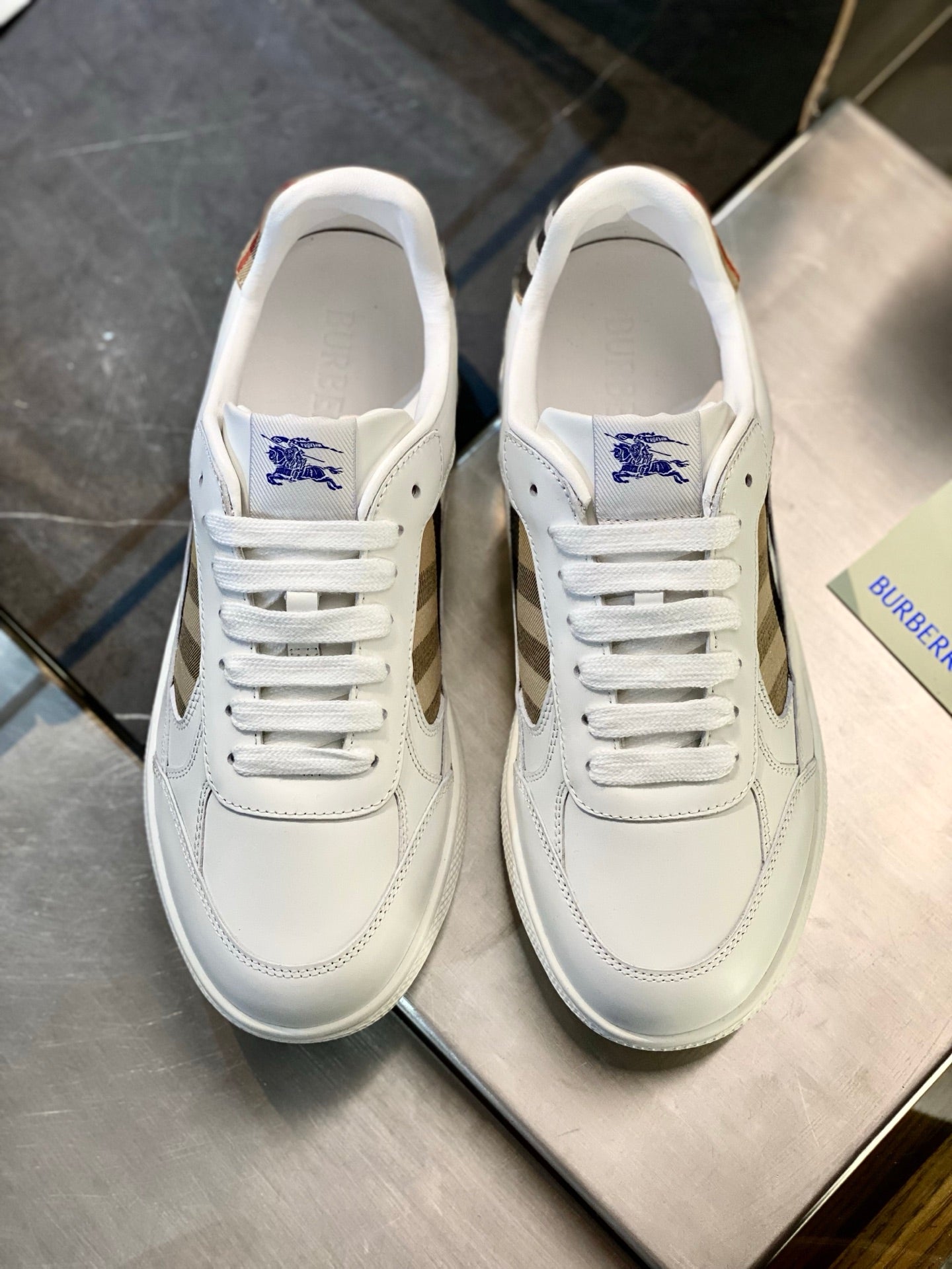 White leather sneakers with blue crest tongue, lace-up front and clean toe shape