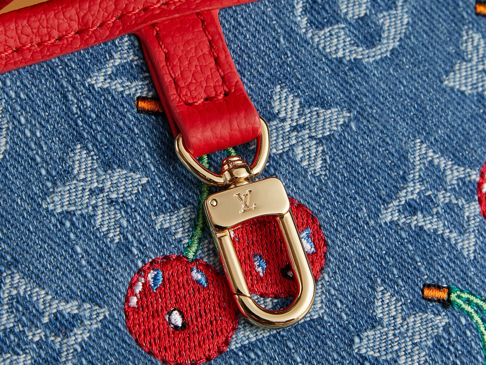 Gold clasp with cherry charm on red strap over denim