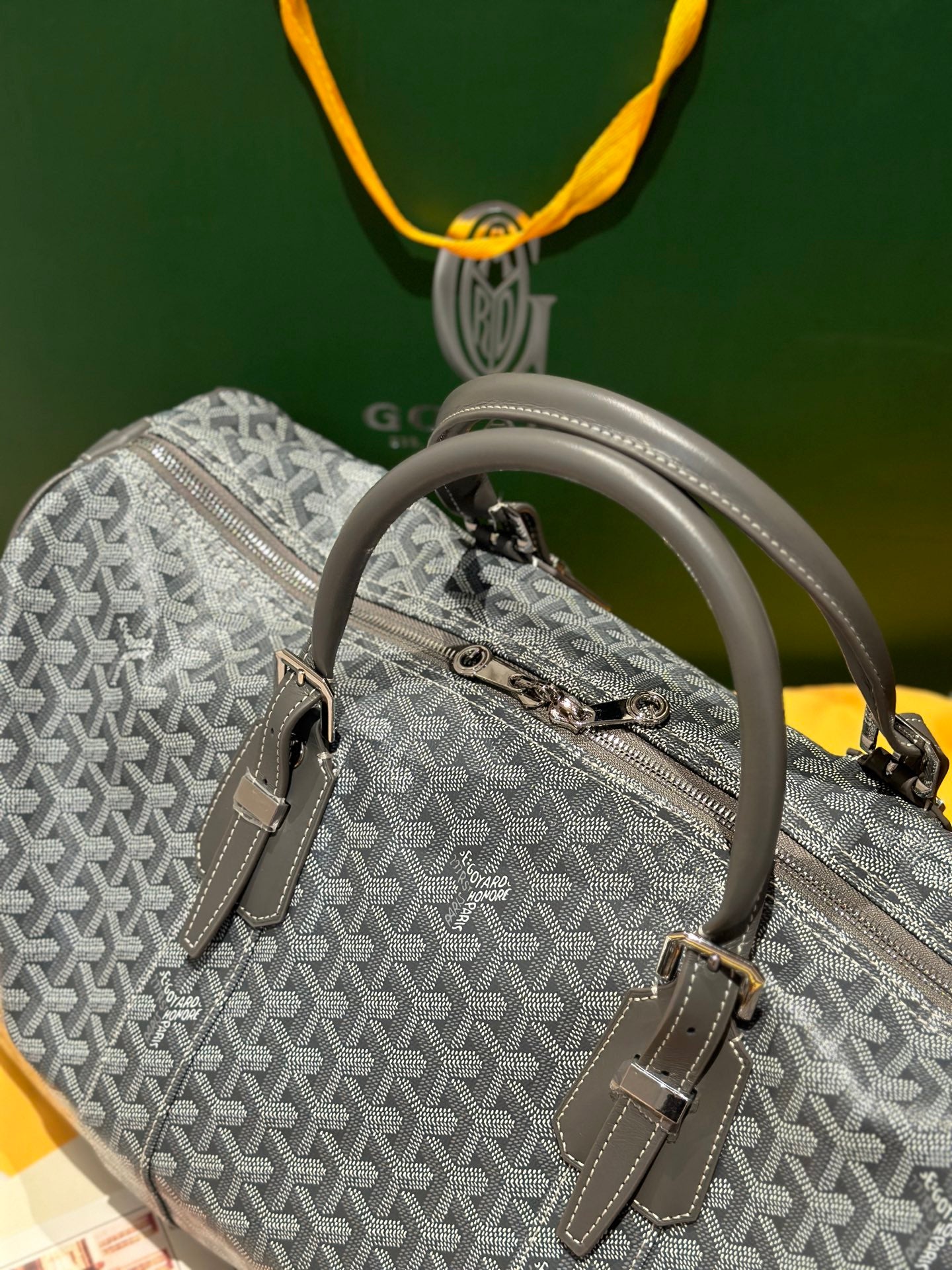 Grey patterned duffel bag with top handle, side buckles, and zip front