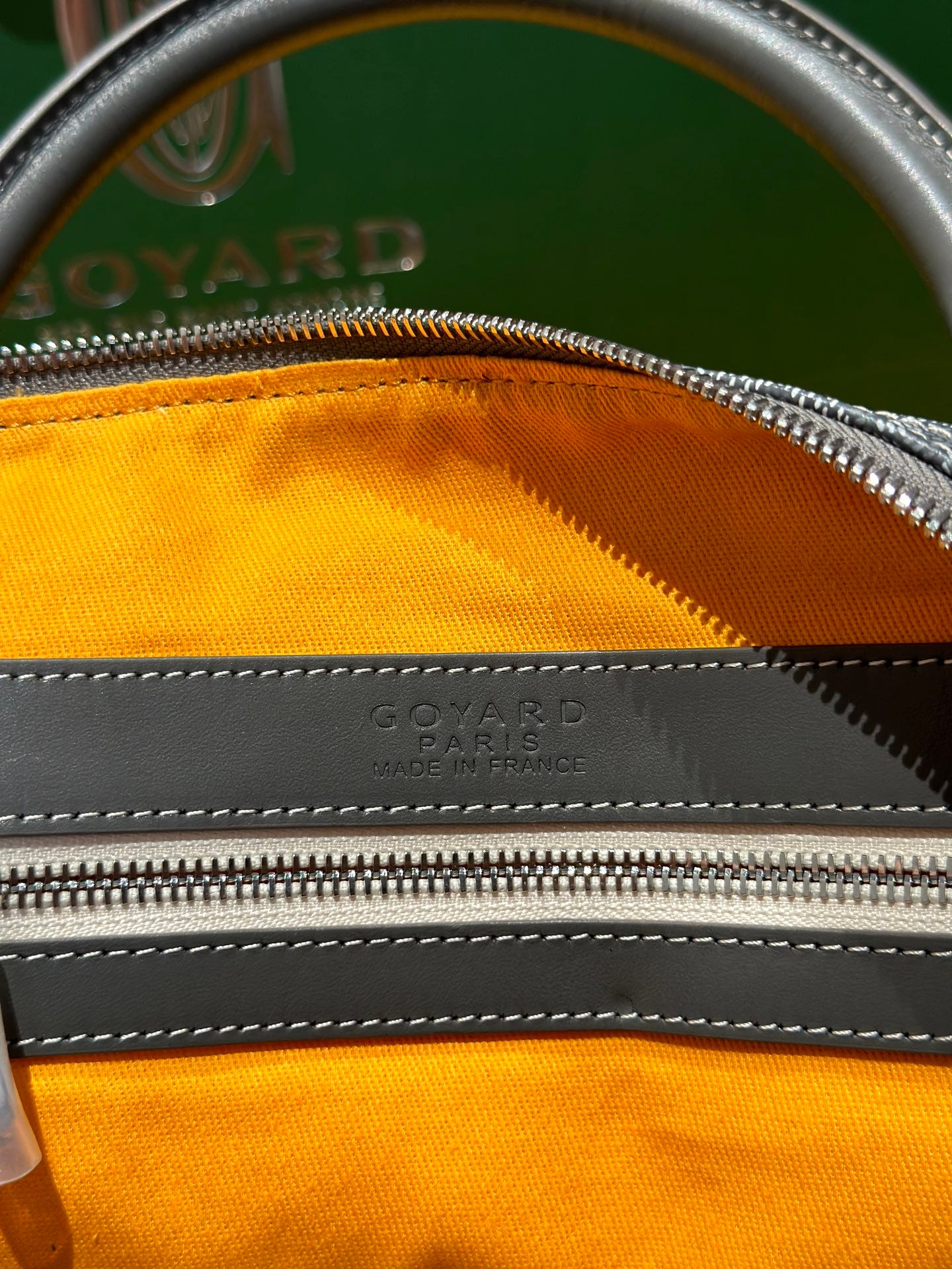 Duﬀel bag top zipper with orange lining and embossed maker mark on leather