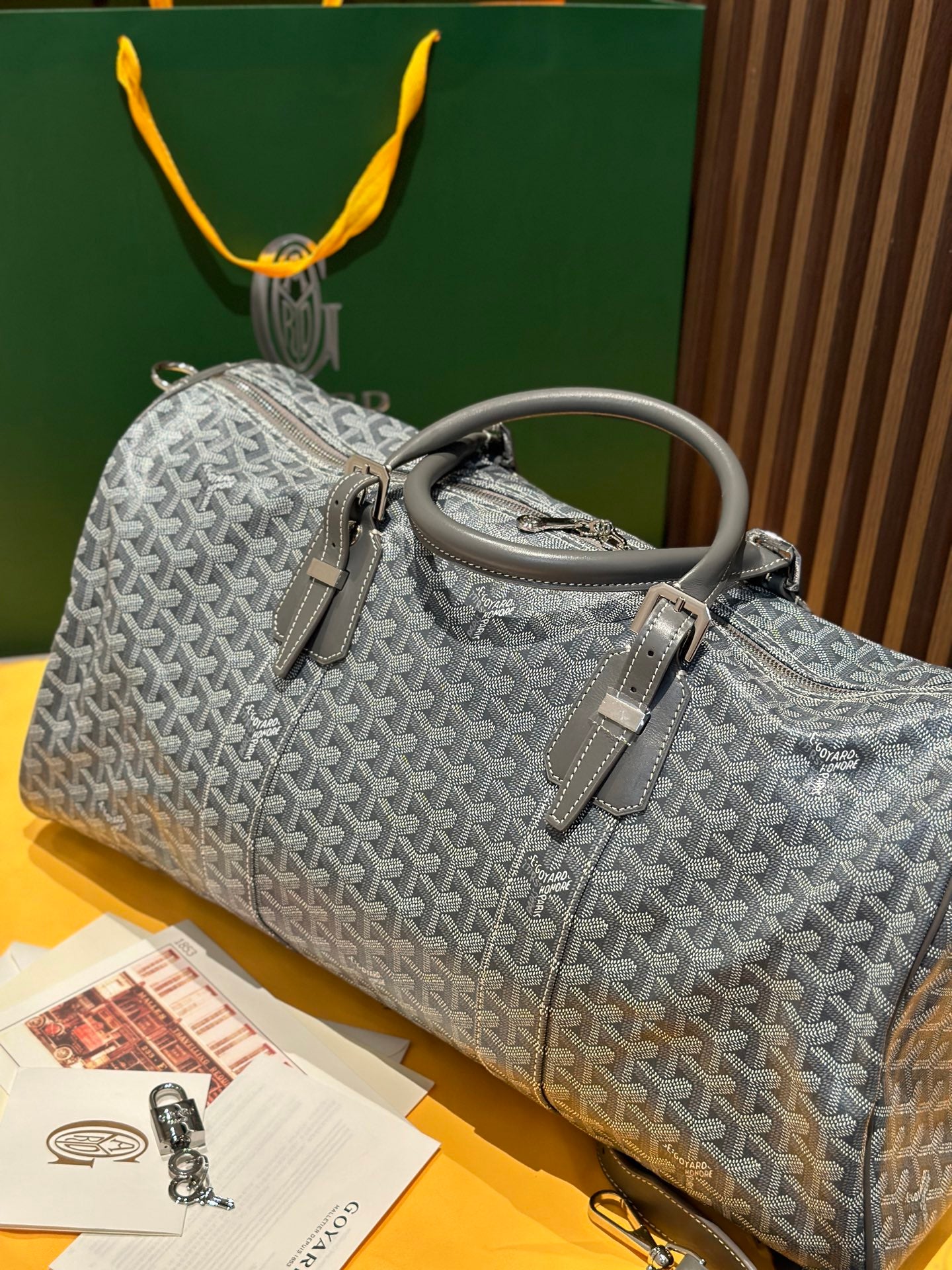 Grey patterned duffel bag with top handles and zip closure, shoulder strap