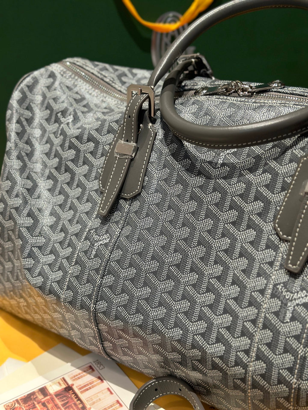 Grey patterned duffel bag with front strap detail, zipper, and top handle