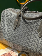 Grey patterned duffel bag with front strap detail, zipper, and top handle