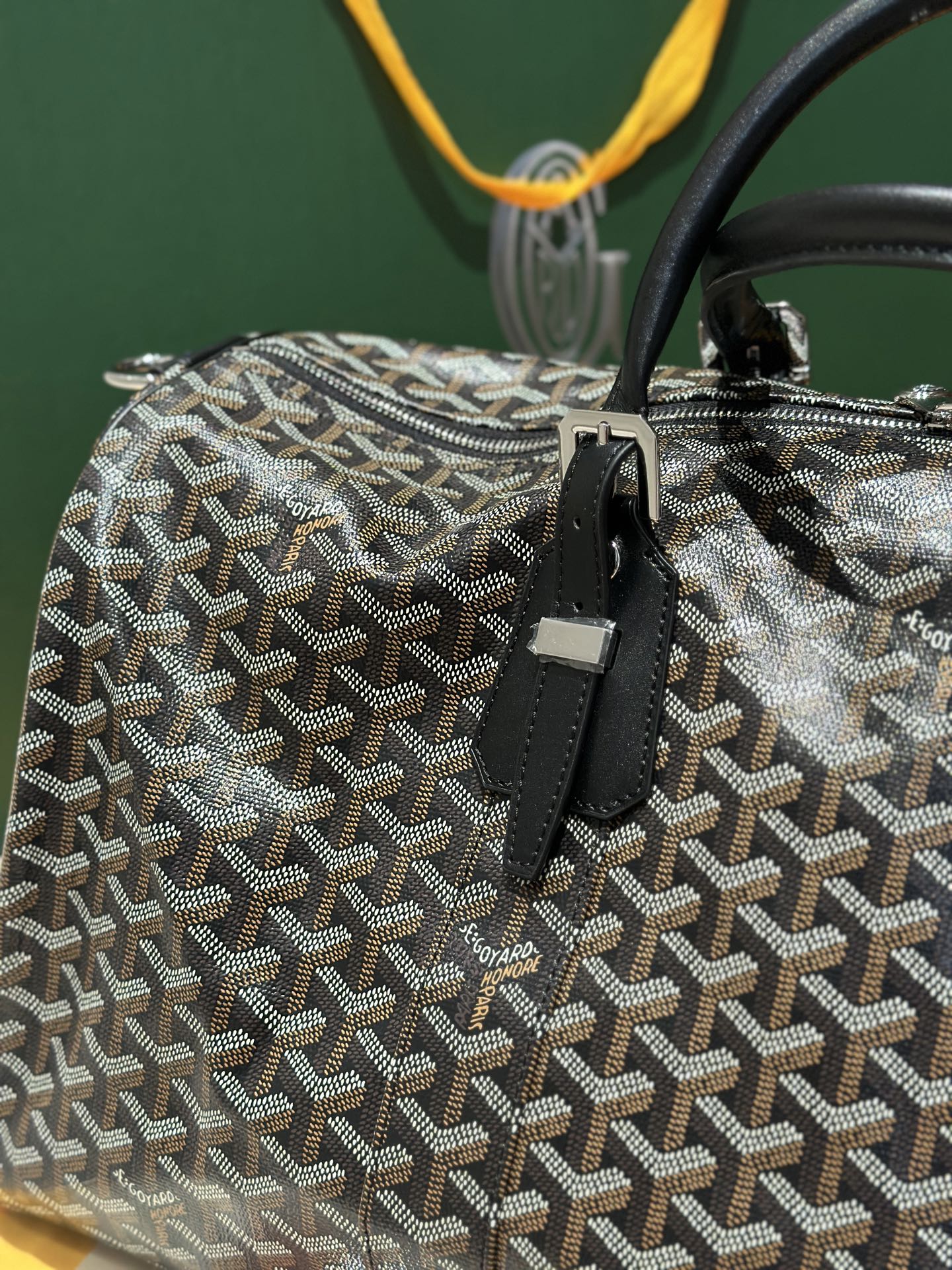 Goyard patterned travel bag close-up with front zipper and black leather strap tab