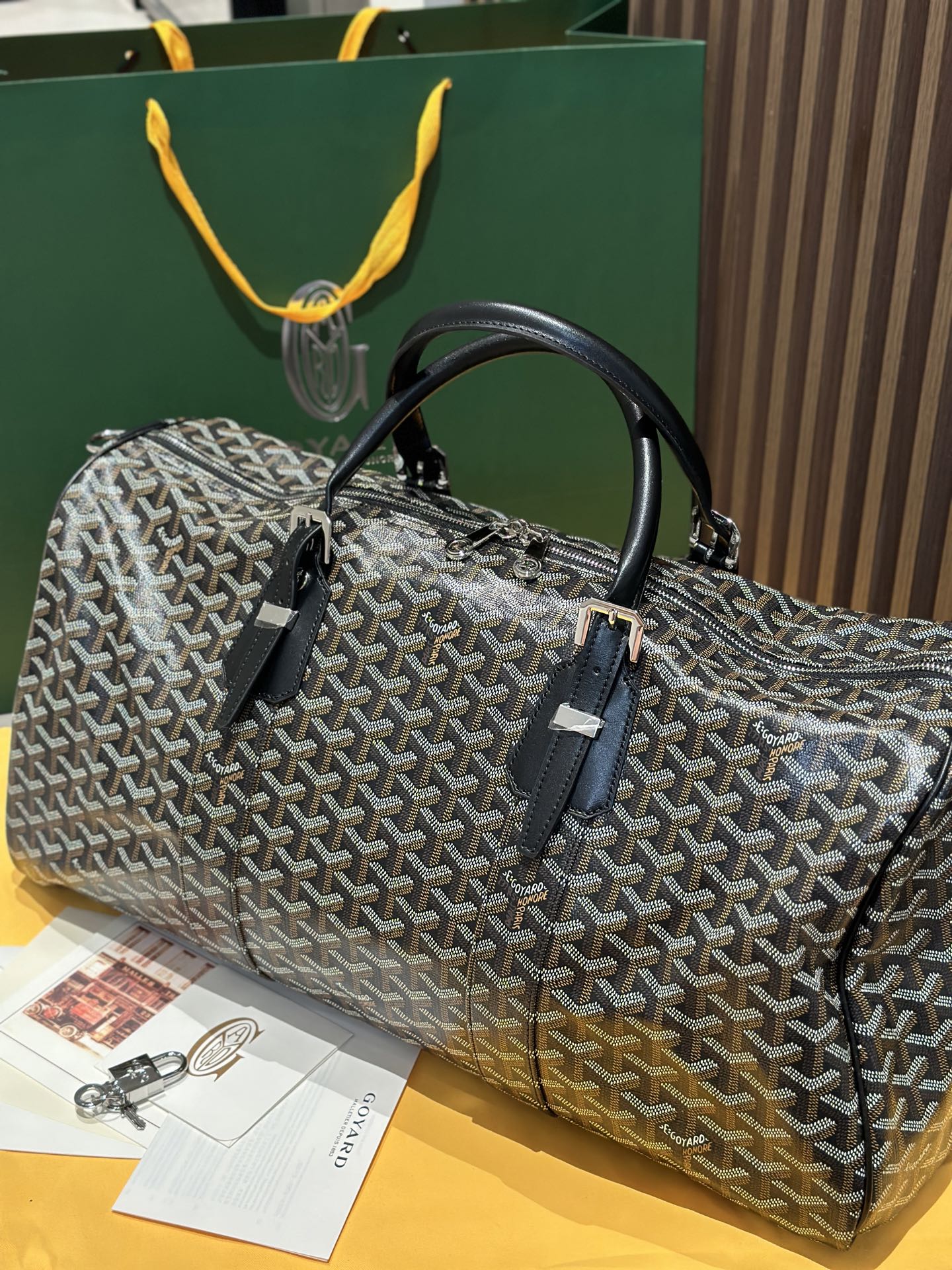 Goyard patterned travel bag front view with black handles and leather accent strap