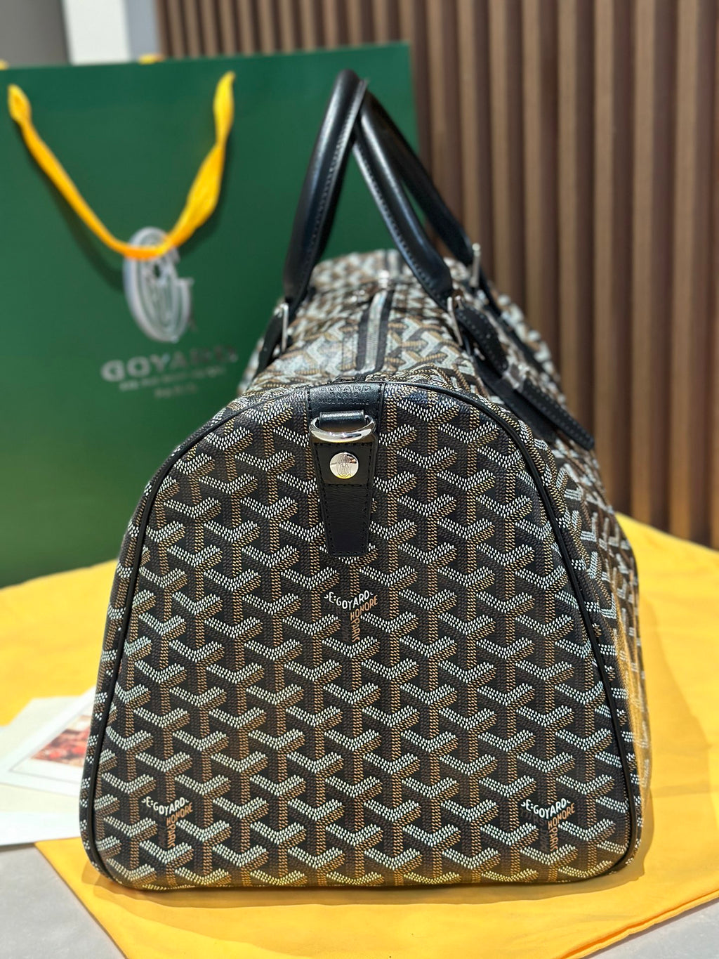 Goyard patterned travel bag with structured body, black handles, and hanging key charm
