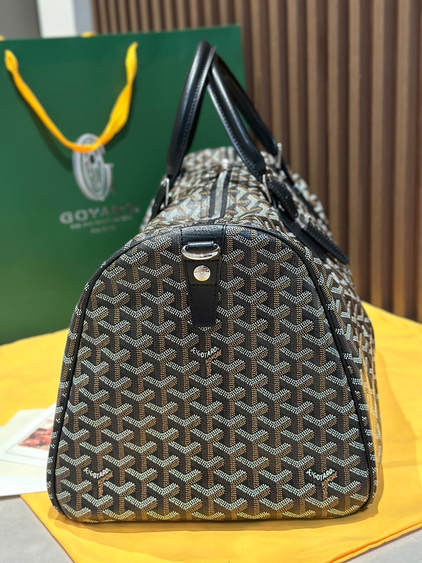 Goyard patterned travel bag with structured body, black handles, and hanging key charm