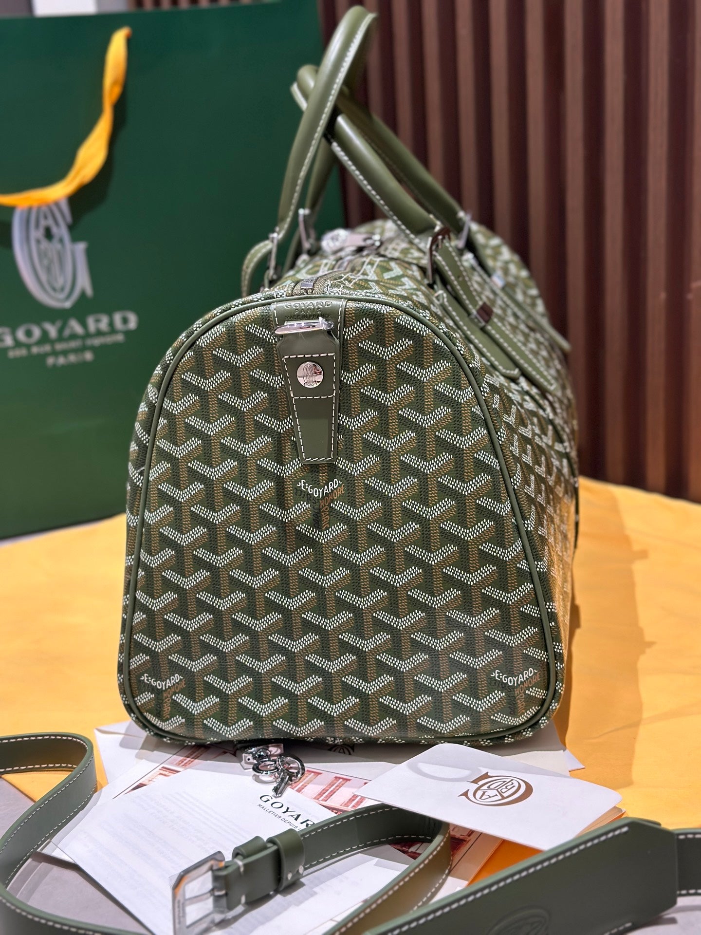 Goyard duffel bag with sage-green Goyardine pattern, rounded handles, and front zipper pocket