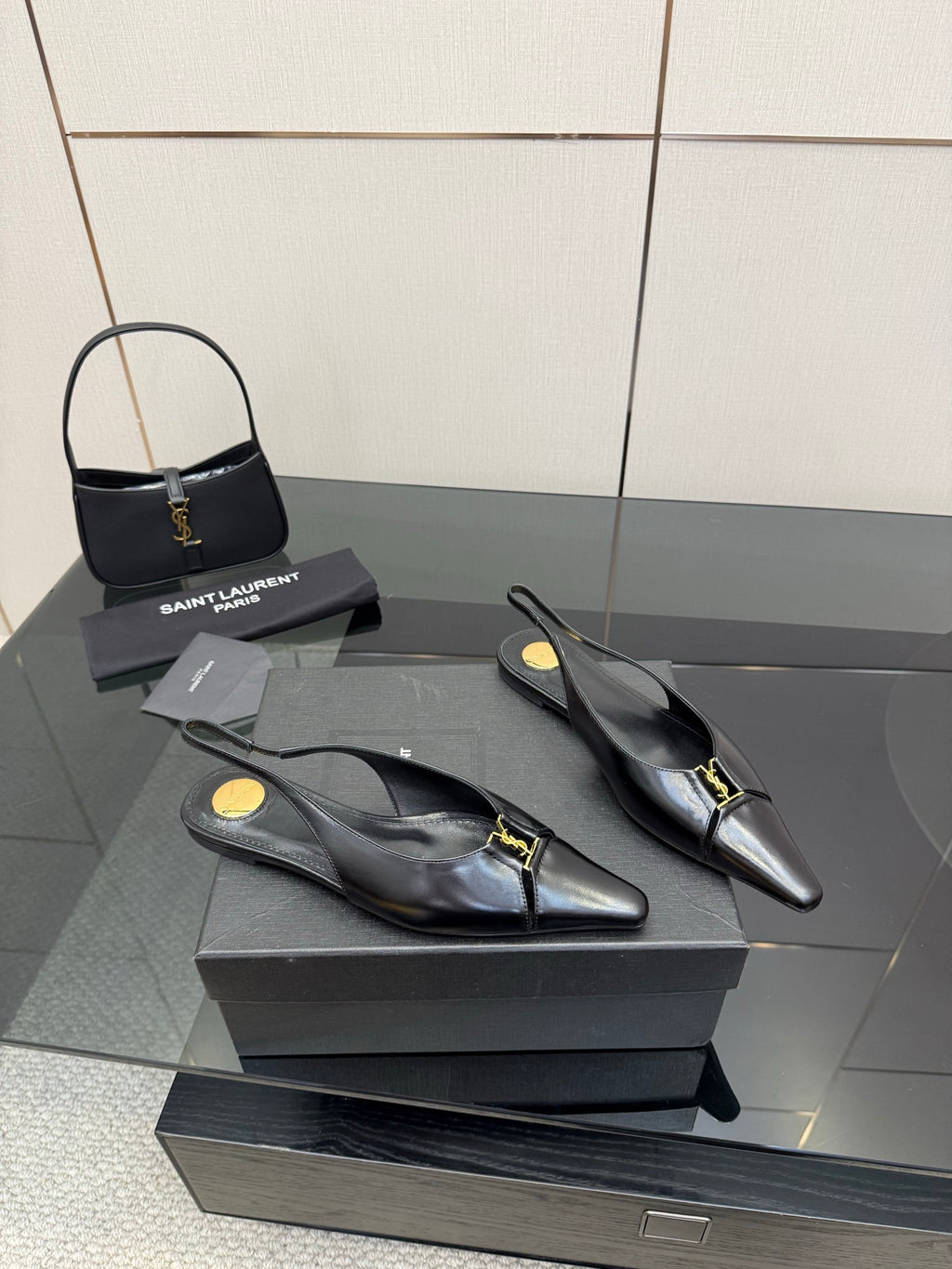 Black pointed-toe slingback heels with gold hardware, side view on the box