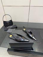 Black pointed-toe slingback heels with gold hardware, side view on the box