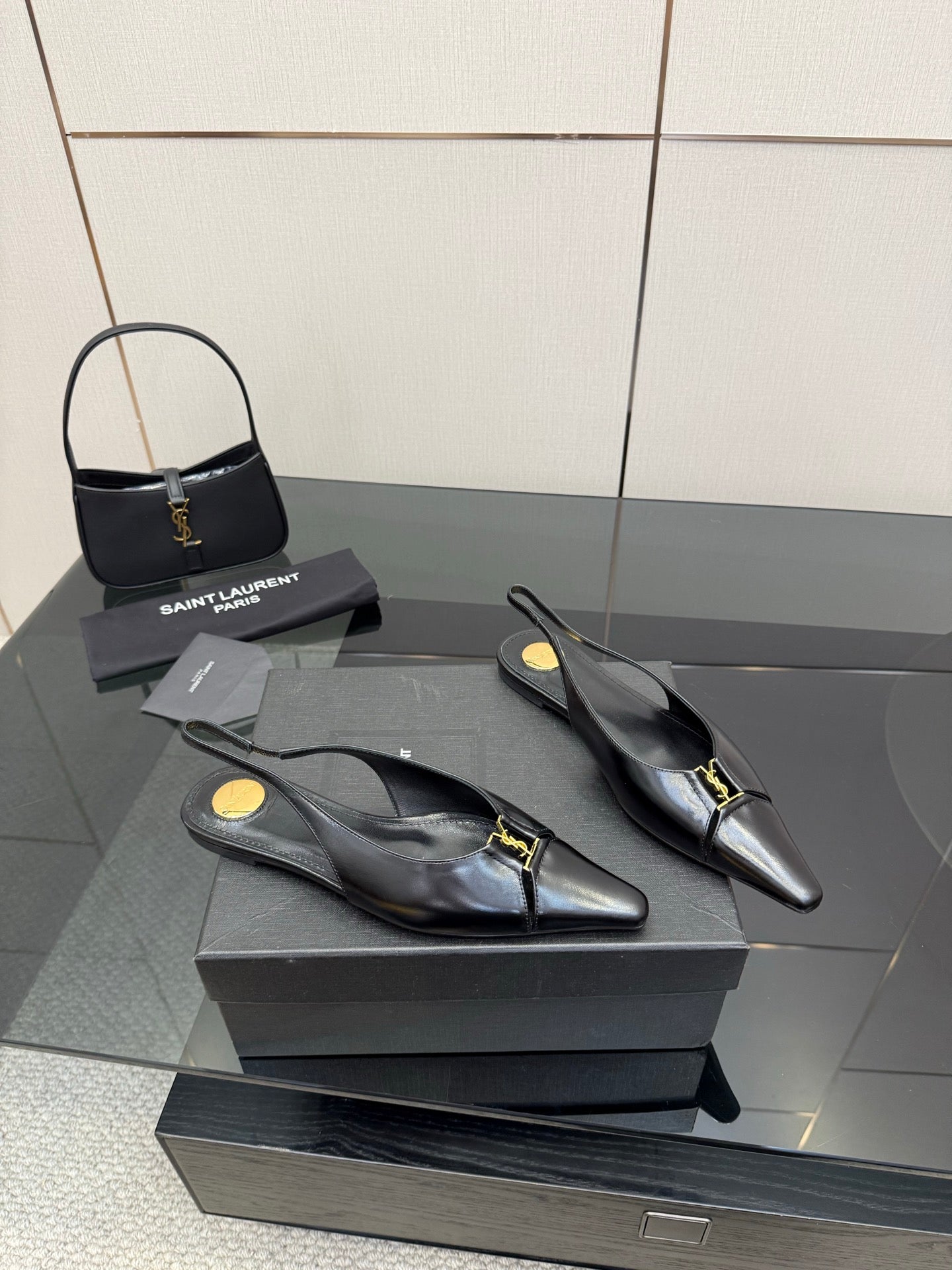 Black pointed-toe slingback heels with gold hardware, side view on the box