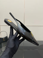Black pointed-toe slingback heel held in hand, gold hardware detail