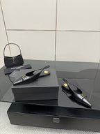 Black pointed-toe slingback heels with gold hardware, pair on dark box