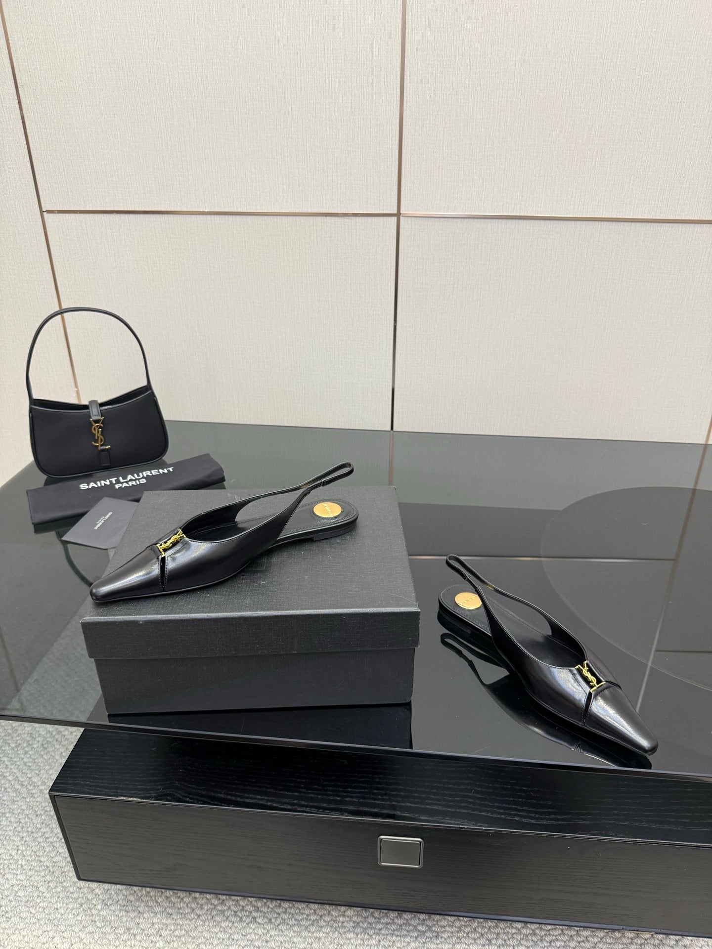 Black pointed-toe slingback heels with gold hardware, pair on dark box