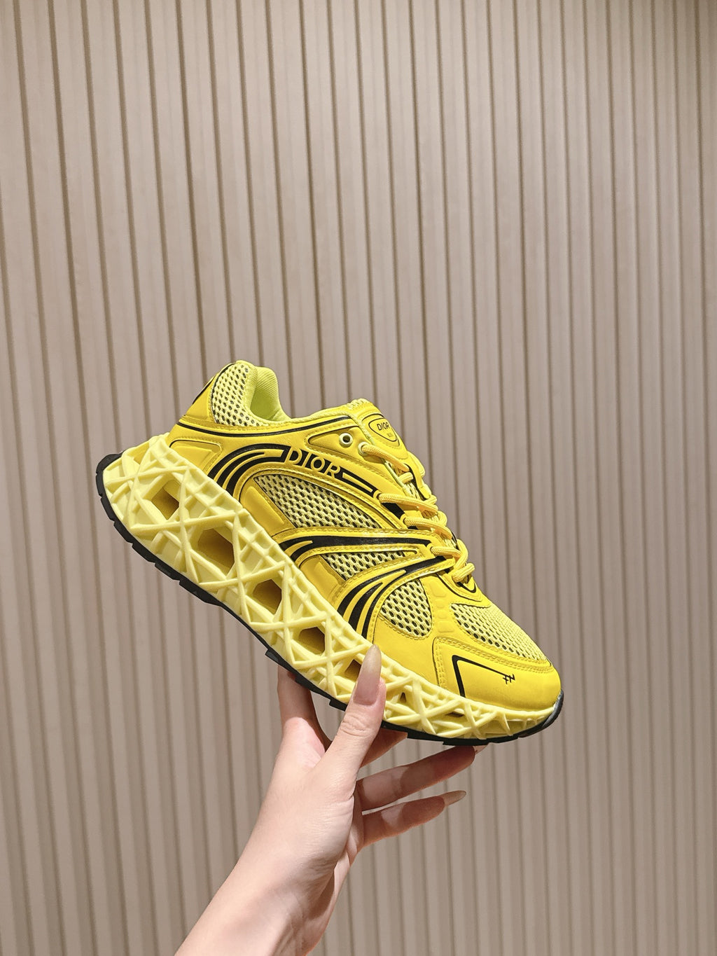 Dior unisex bright yellow sneaker held in hand, side profile with logo and laces