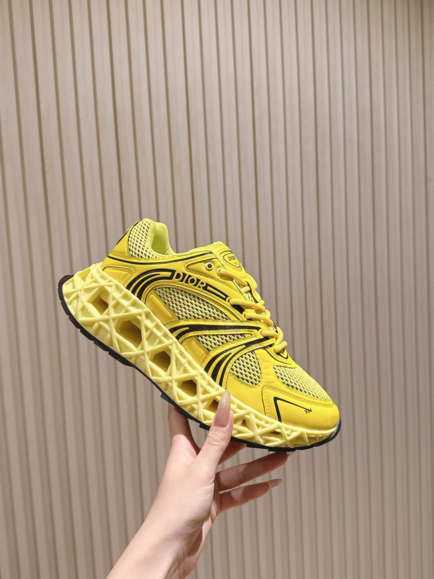 Dior unisex bright yellow sneaker held in hand, side profile with logo and laces