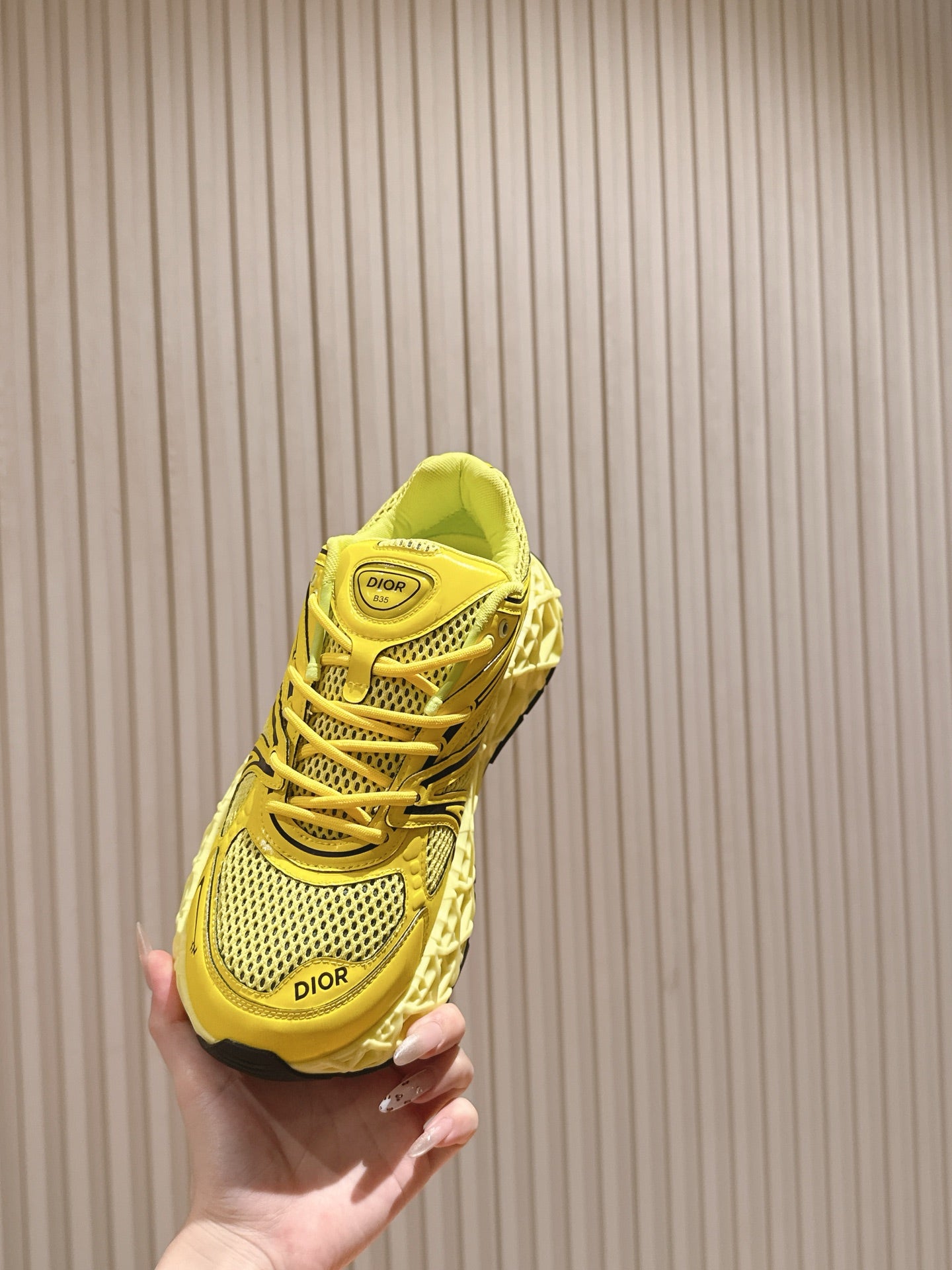 Dior unisex bright yellow sneaker held in hand, rear view with heel panel