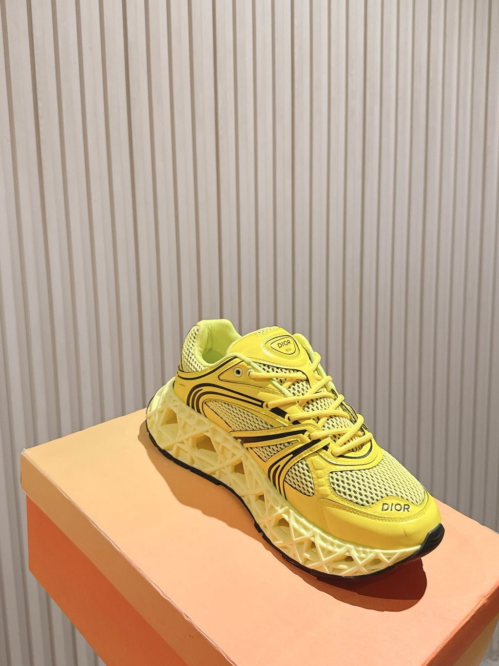 Dior unisex bright yellow low-top sneakers on a light orange box, side view