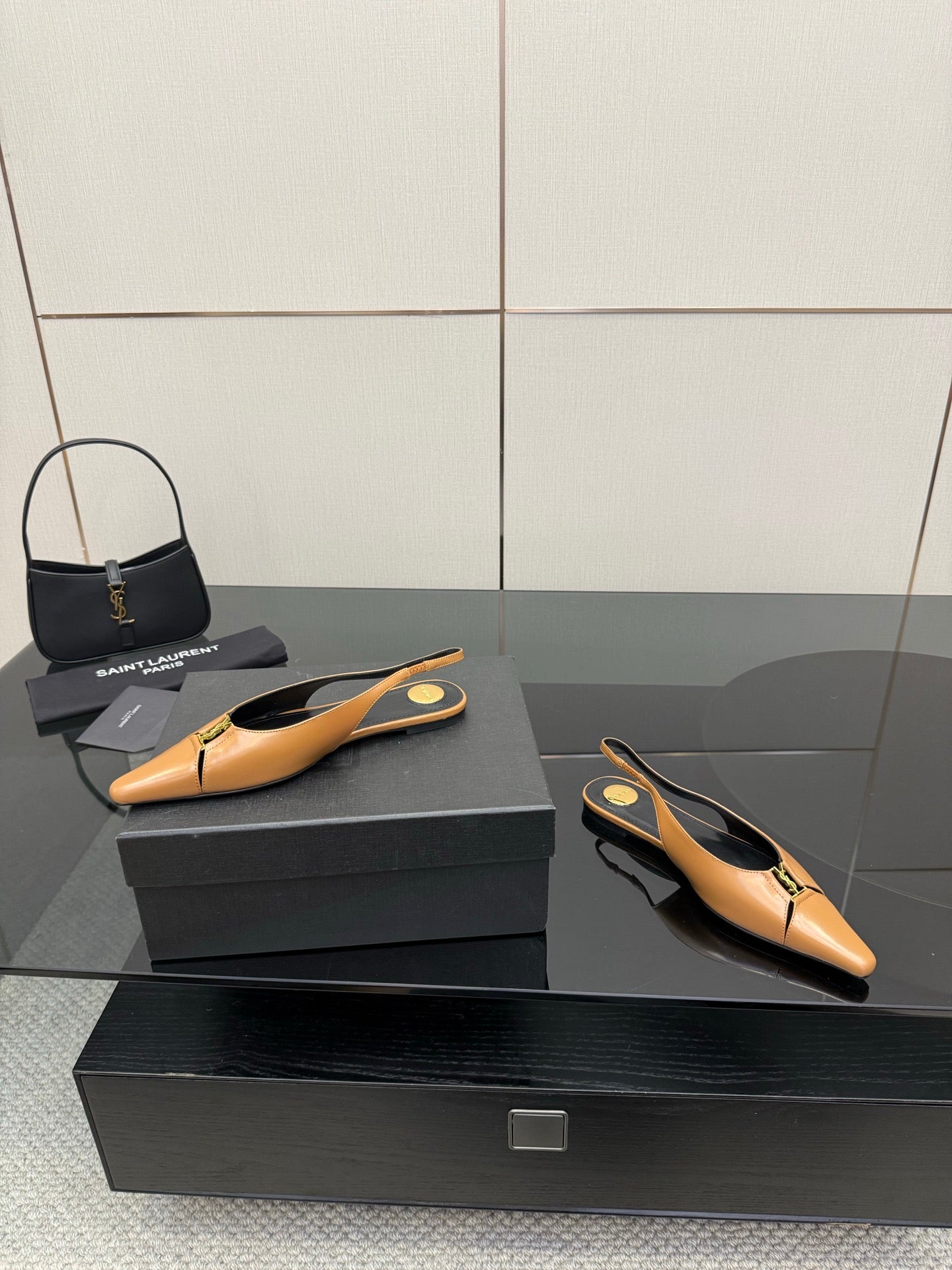 Tan pointed-toe slingback flats displayed on black shoe boxes, black lining and gold logo