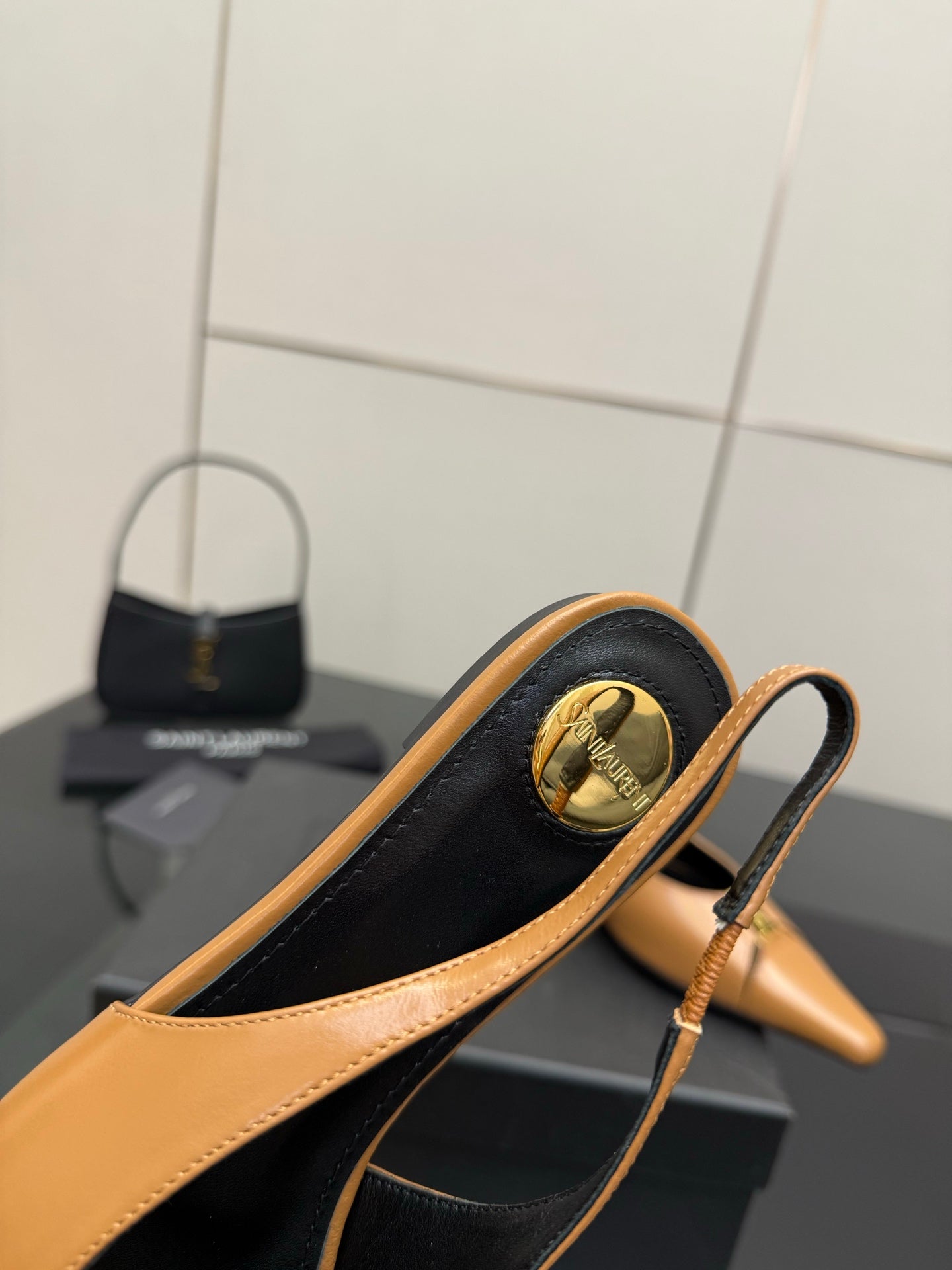Tan pointed-toe slingback flat heel strap with gold round emblem and black interior lining