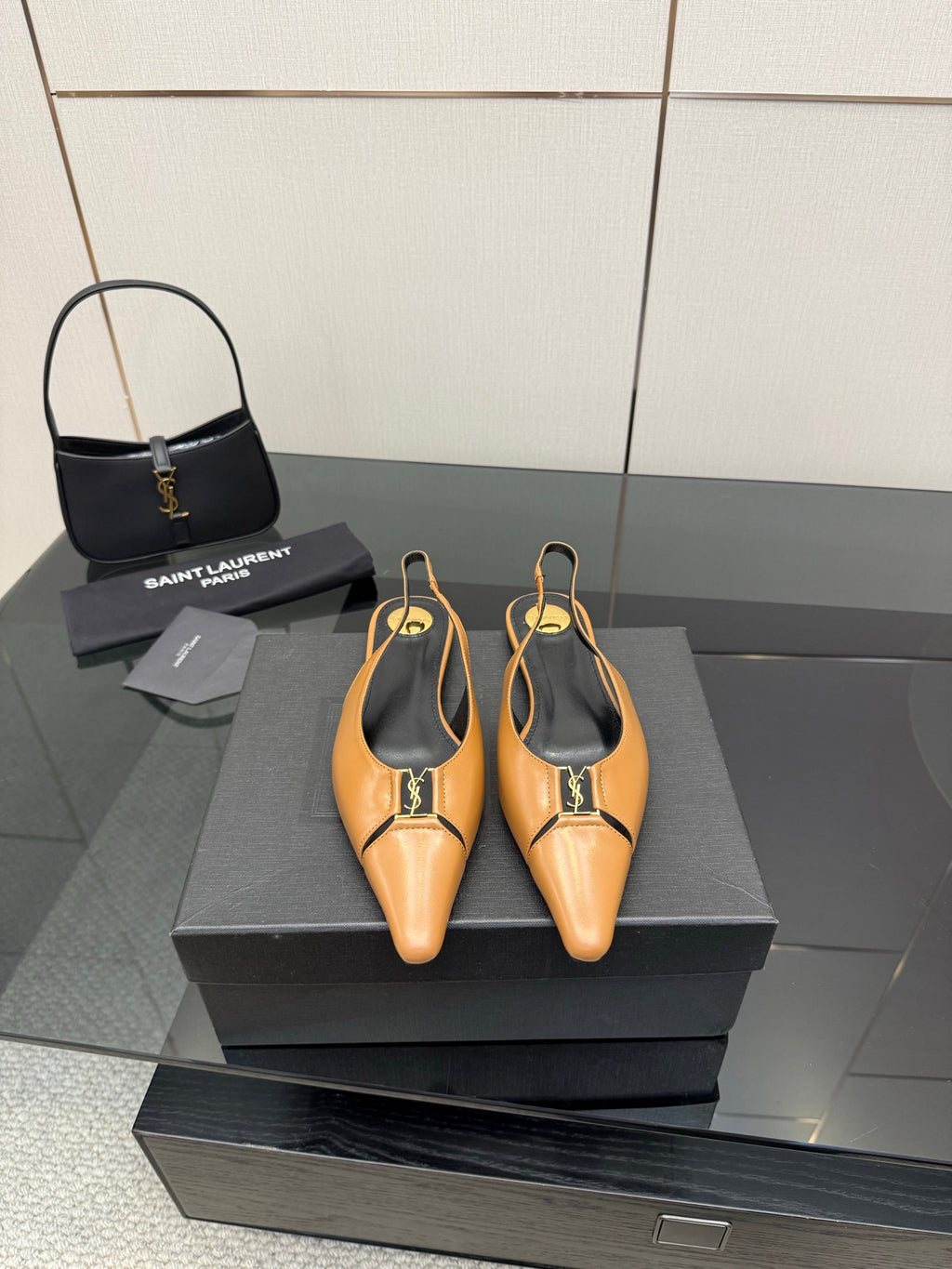 Pair of tan pointed-toe slingback flats with black lining and gold logo hardware