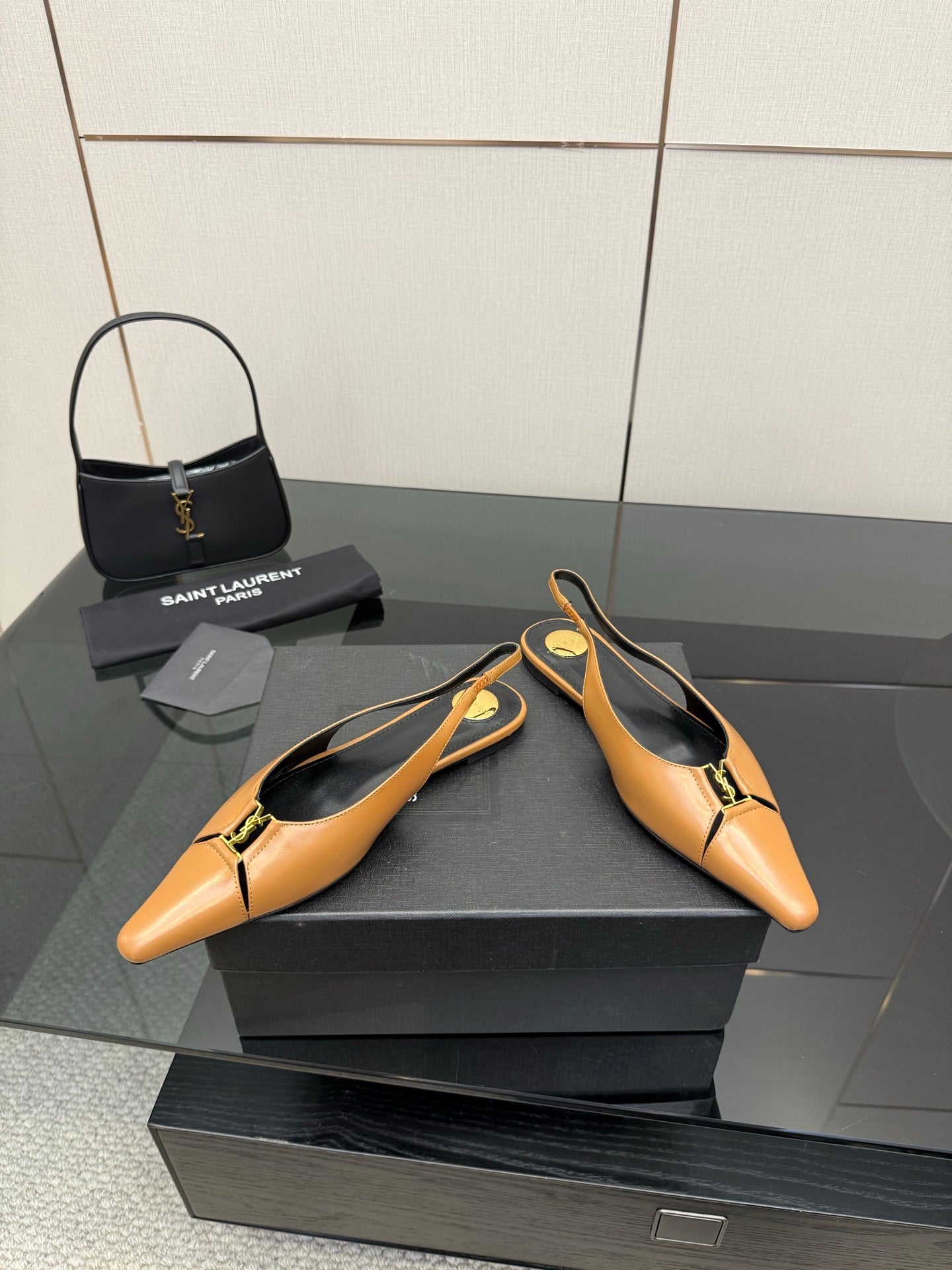 Two tan pointed-toe slingback flats with black lining and gold logo hardware, front view