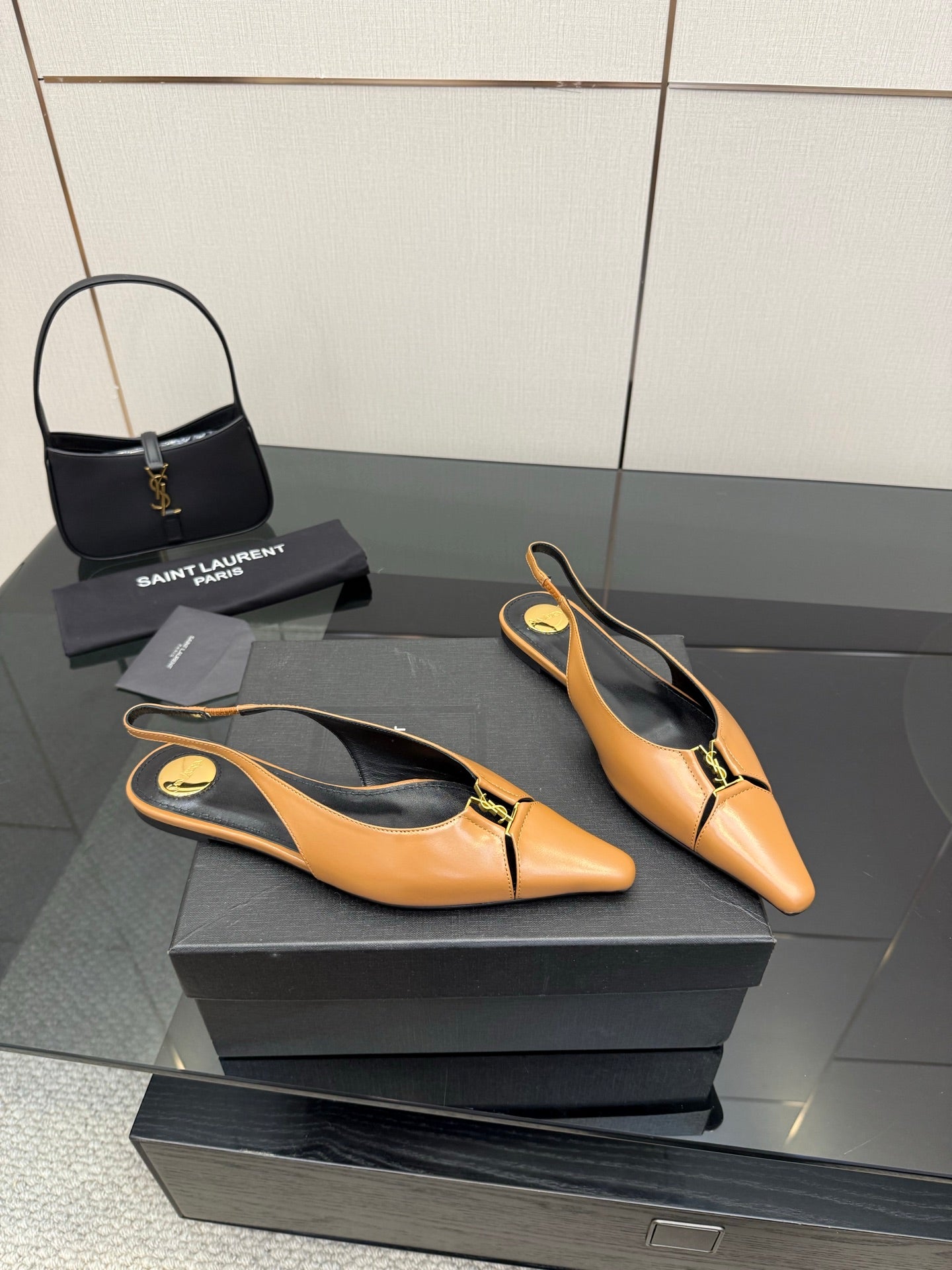 Tan pointed-toe slingback flats on a shoe box, black lining, gold logo accents