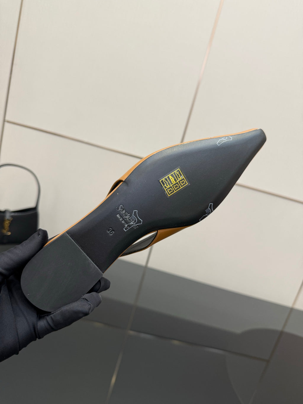 Black heel underside of a slingback flat with gold emblem branding on the footbed