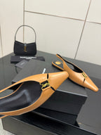 Close-up of tan pointed-toe slingback flat with black interior and gold logo strap detail