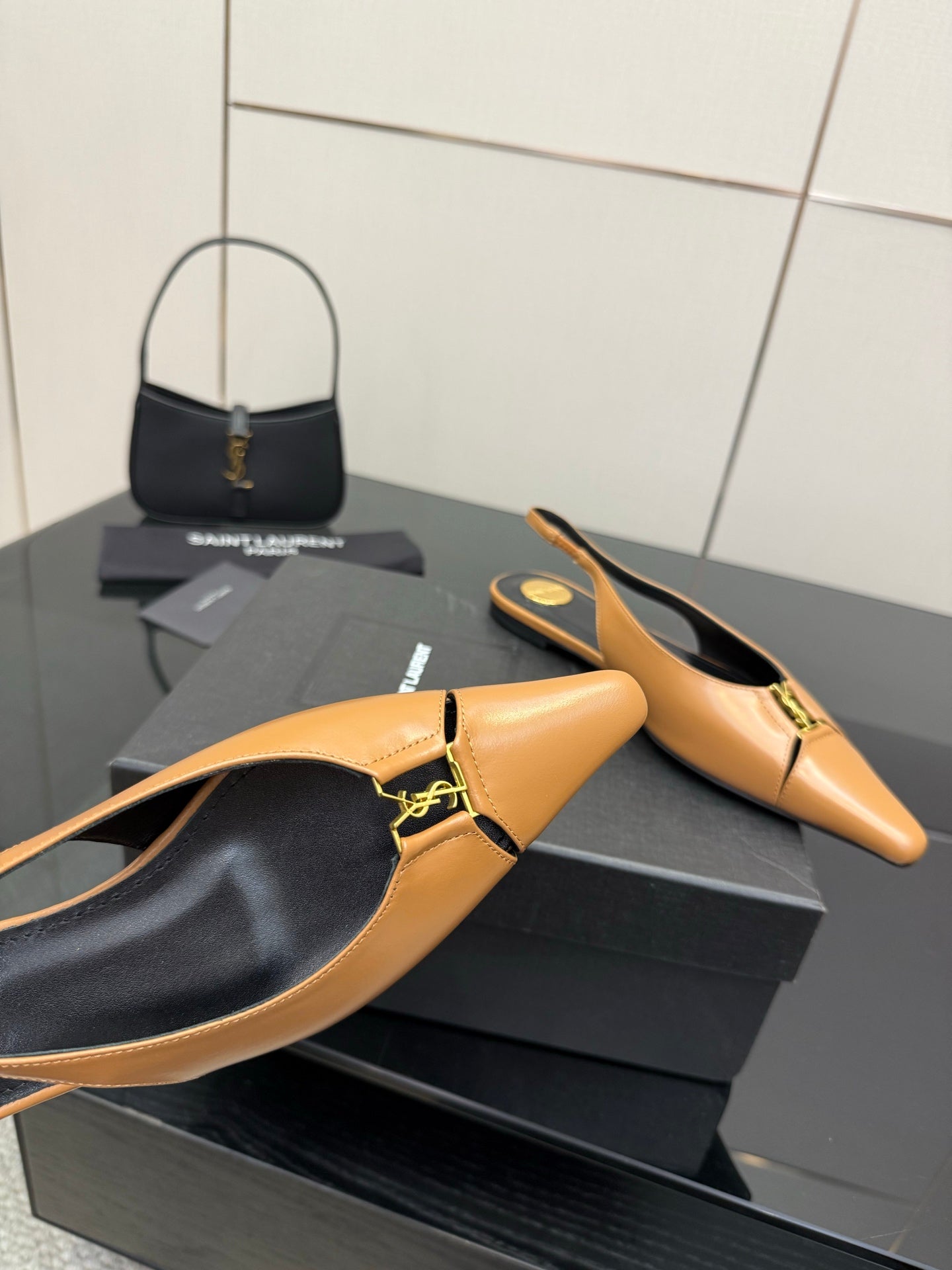 Close-up of tan pointed-toe slingback flat with black interior and gold logo strap detail
