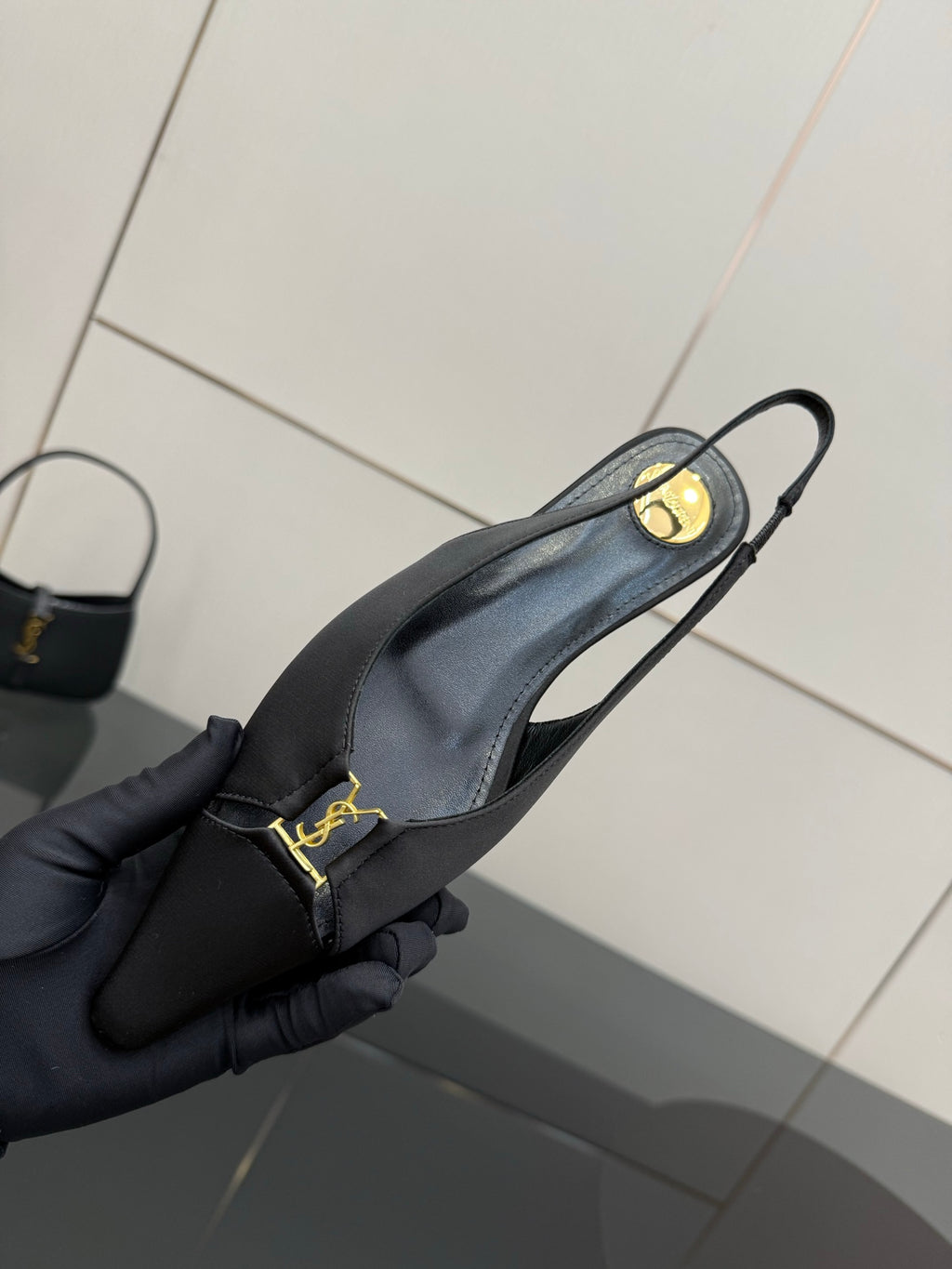 Women's black slingback heel held in hand, gold logo strap at ankle