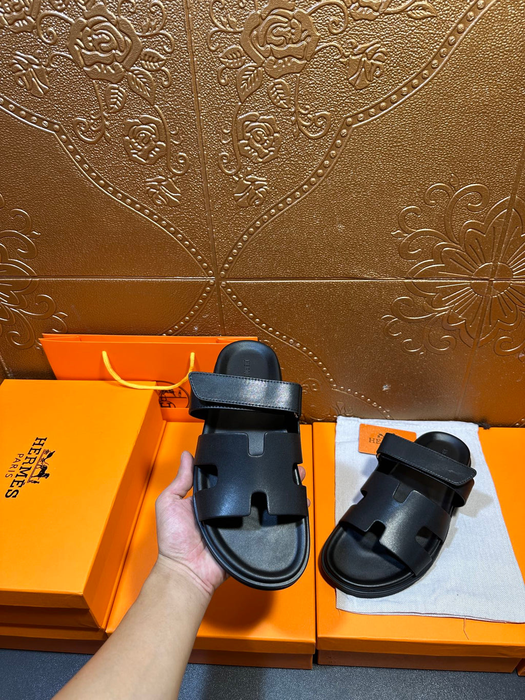 Hermes dark leather slide sandals in hand, double straps visible