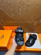 Hermes dark leather slide sandals in hand, double straps visible