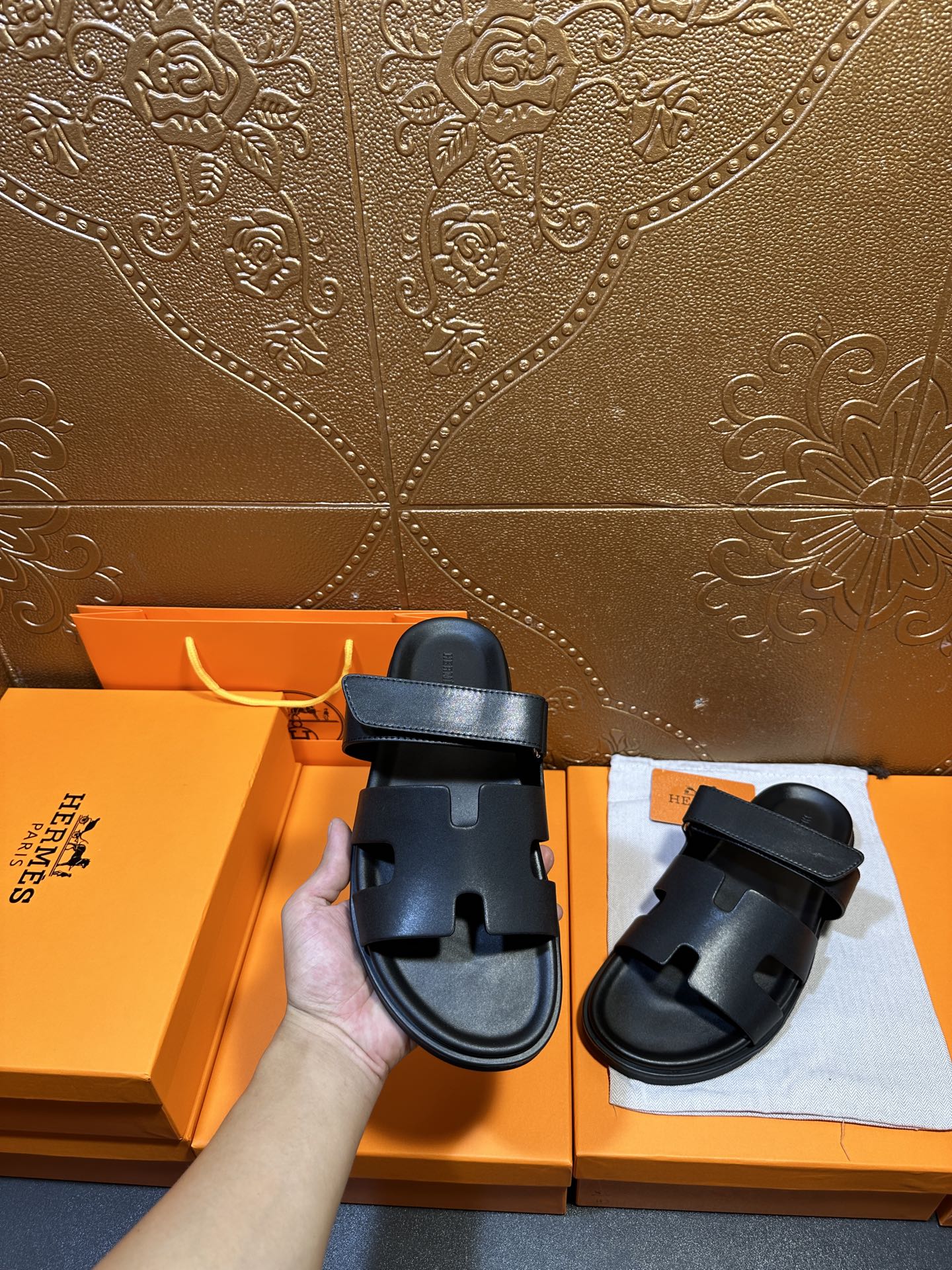 Hermes dark leather slide sandals in hand, double straps visible