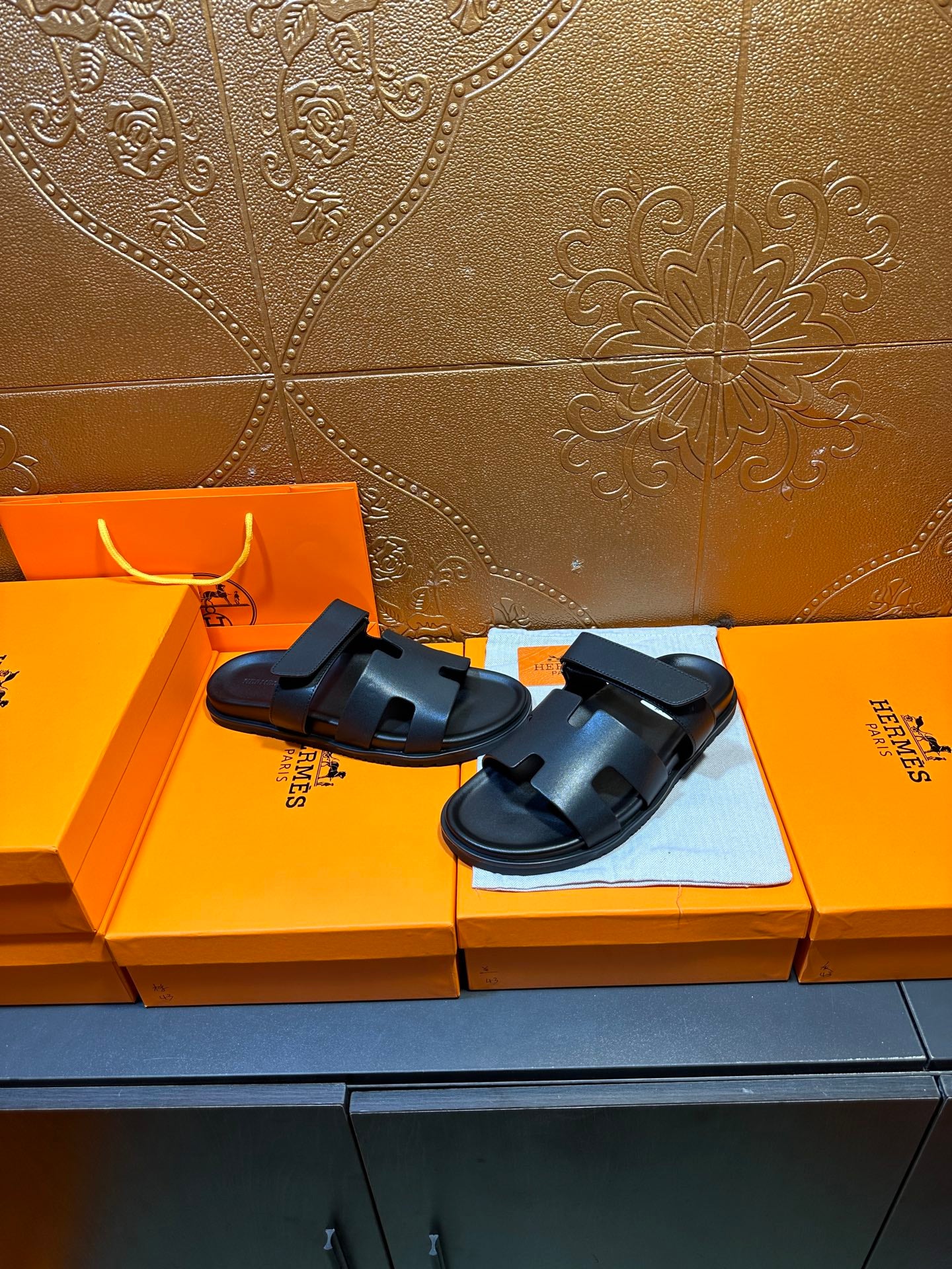 Hermes dark leather slide sandals with double straps, resting on display surface