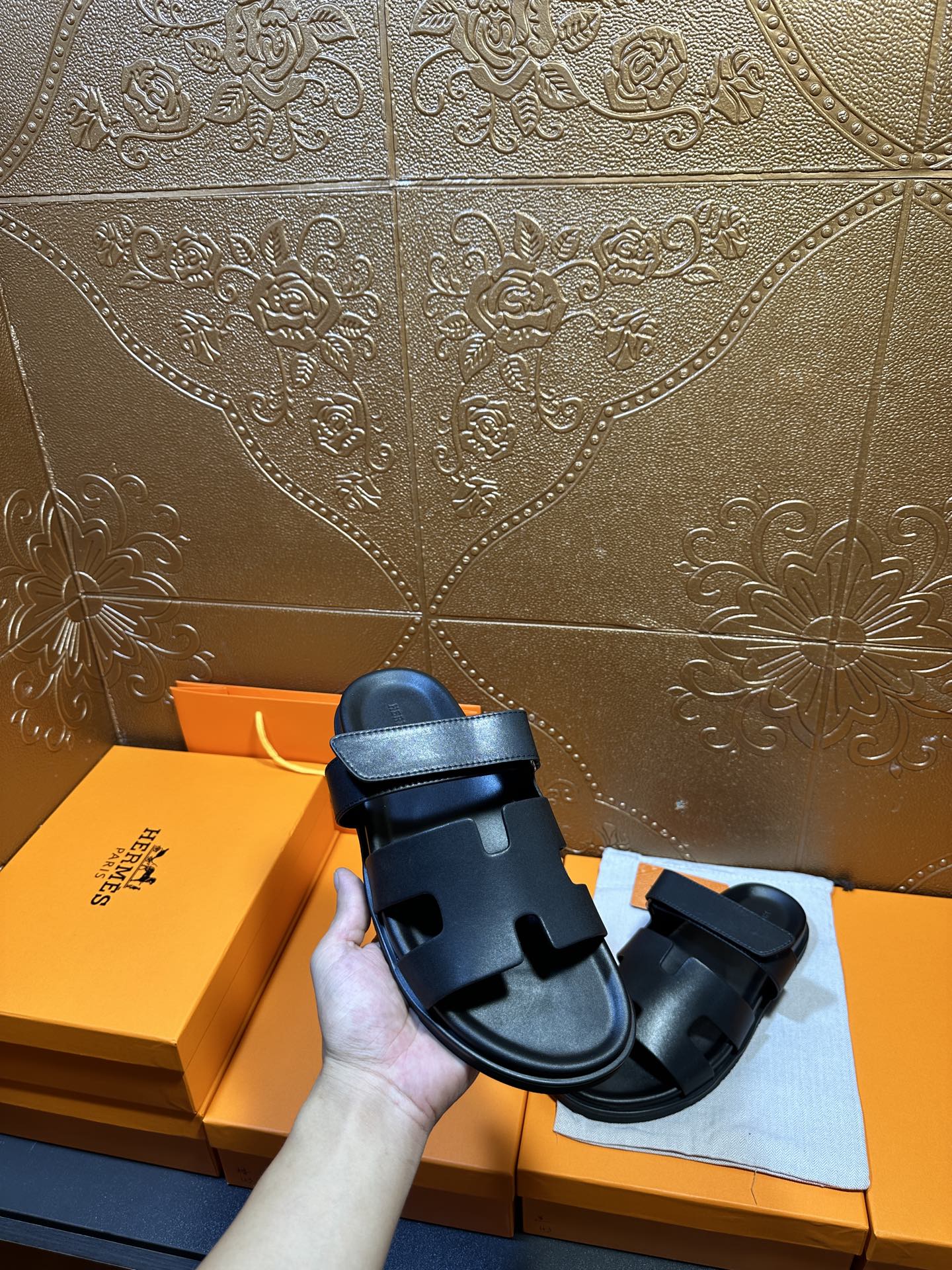 Hermes dark leather slide sandal held up, showing double strap design