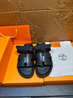 Hermes dark leather slide sandals with double straps, shown as a pair
