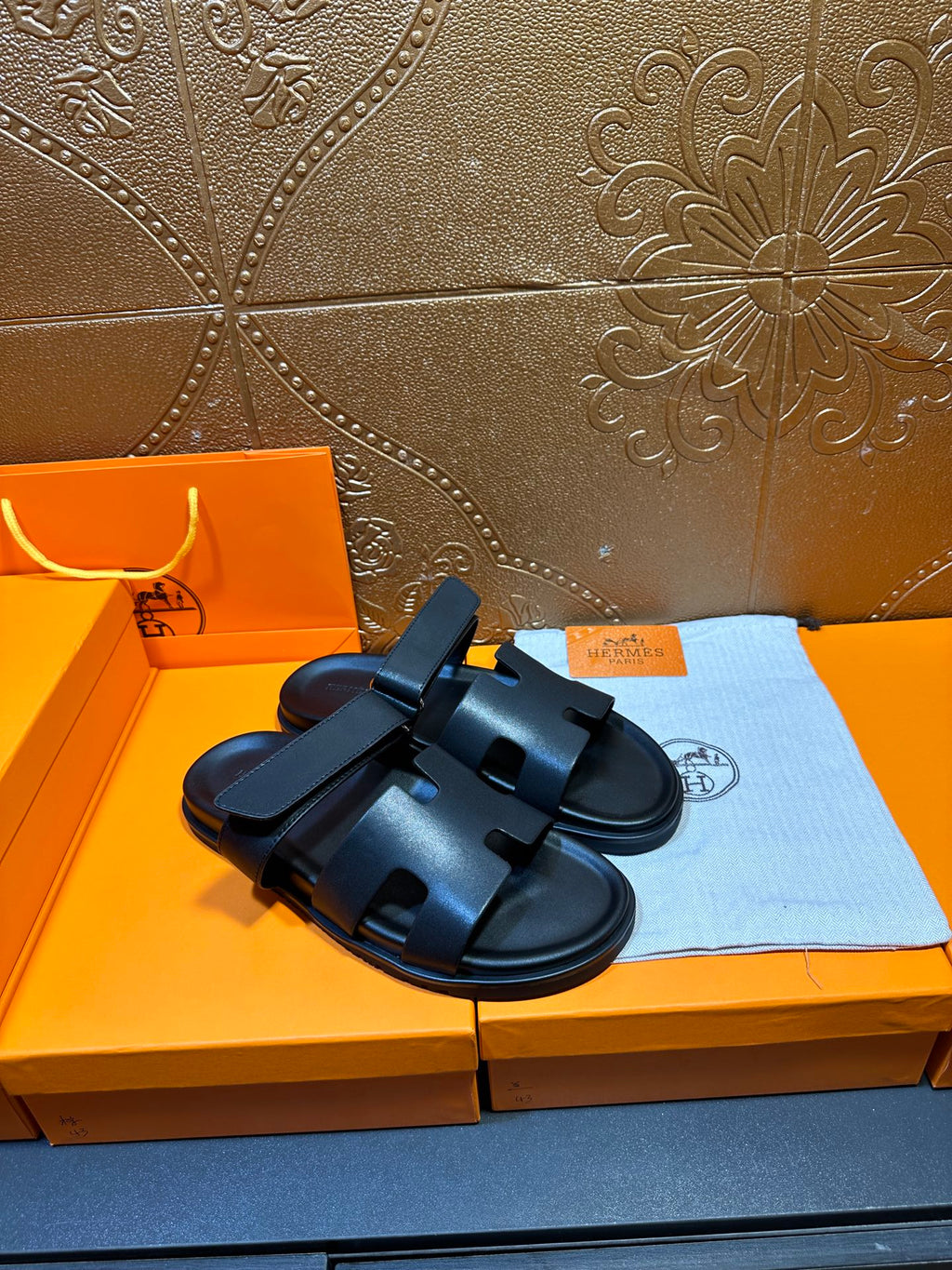 Hermes dark leather slide sandals with double straps, side-by-side on box