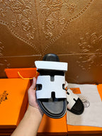 White slide sandals with black sole and decorative strap cutouts