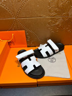 Pair of white slide sandals with black soles and H-shaped strap cutouts