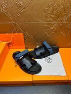 Hermes black slide sandals with blue strap, angled view with dust bag