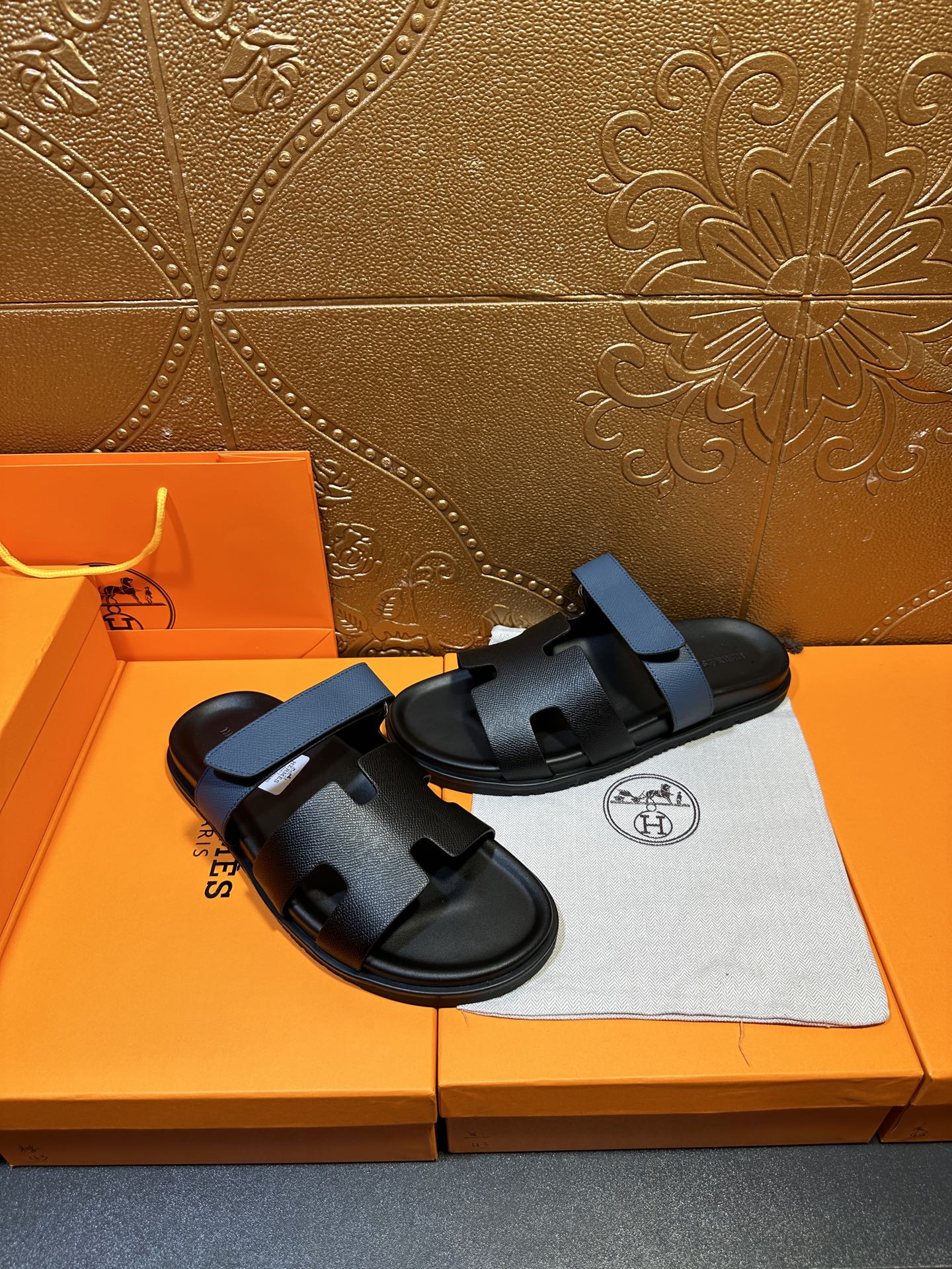Hermes black slide sandals with blue strap, angled view with dust bag