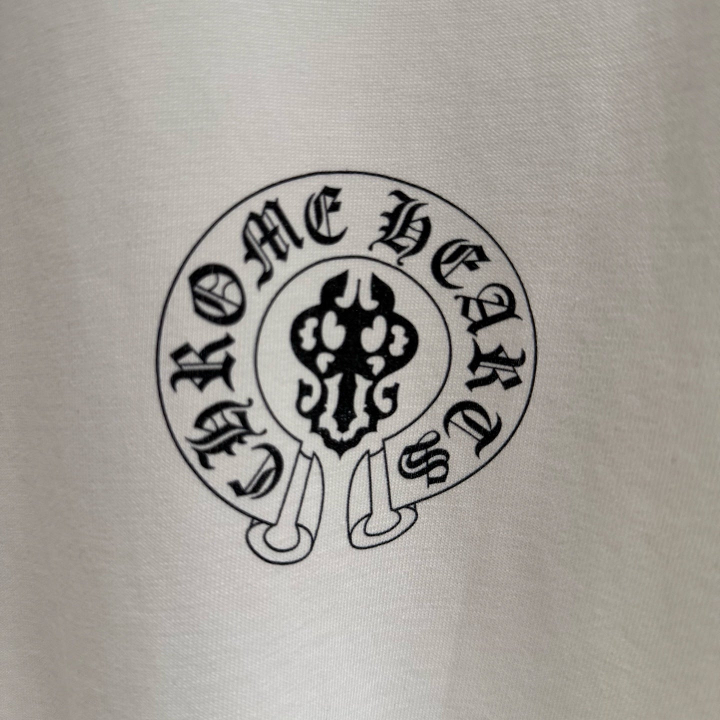 Close-up of circular “Chrome Hearts” emblem print on a white T-shirt